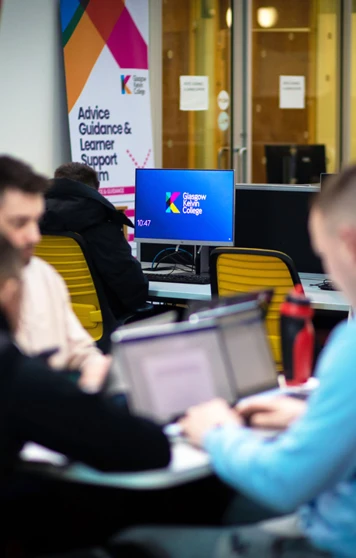 Students working together on laptops in a pod area at Glasgow Kelvin College, with a support services banner and desktop monitors in the background. Students working together on laptops in a pod area at Glasgow Kelvin College, with a support services banner and desktop monitors in the background.